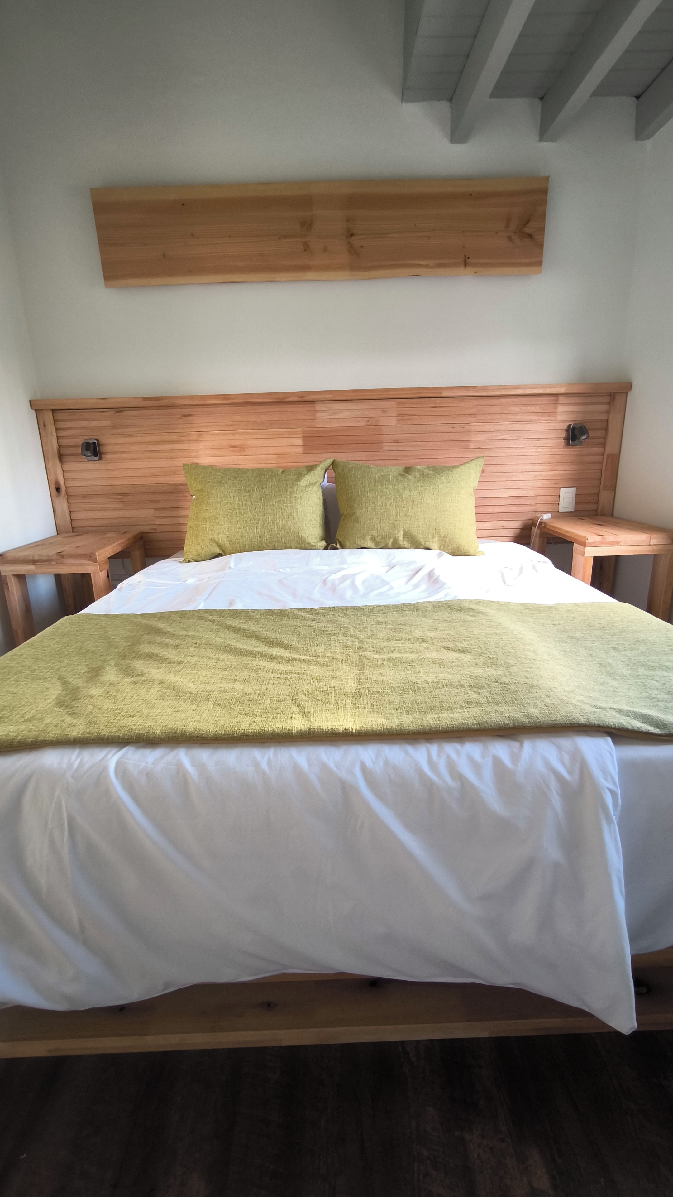 Una cama con cabecera de madera, dos almohadas y una manta verde.