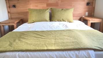 Una cama con cabecera de madera, dos almohadas y una manta verde.