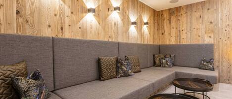 A modern interior with a wooden wall panel, grey upholstered seating, and round tables.