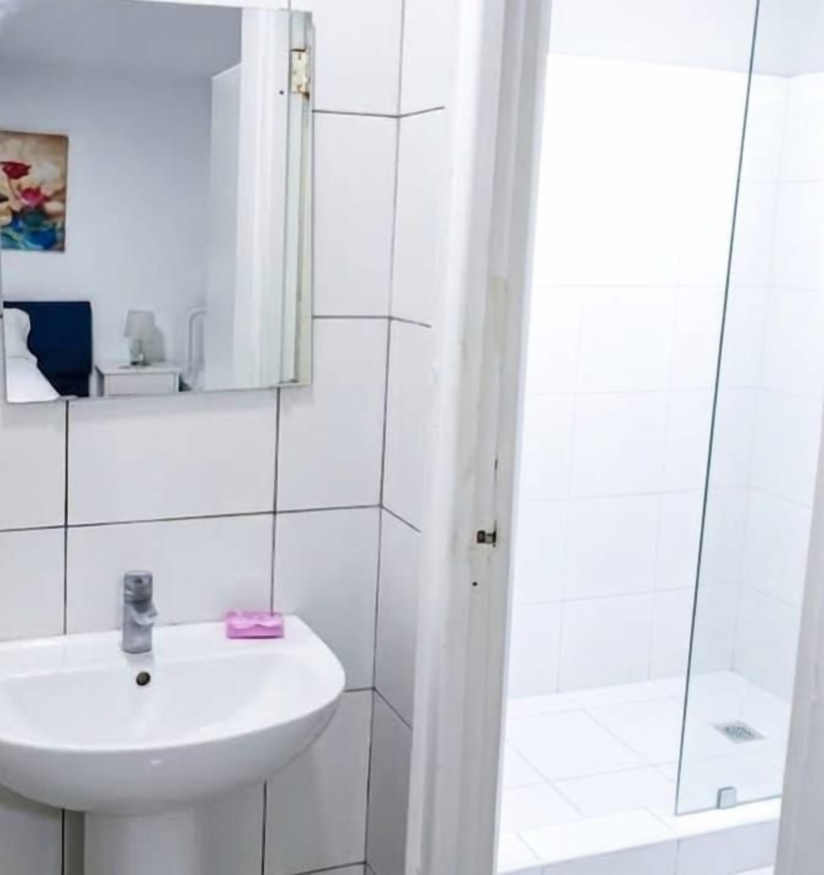 Een badkamer met een witte wastafel, een spiegel en een douche met glazen wanden.