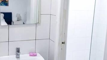 Casa de banho com lavatório branco, espelho e cabine de duche com vidro.