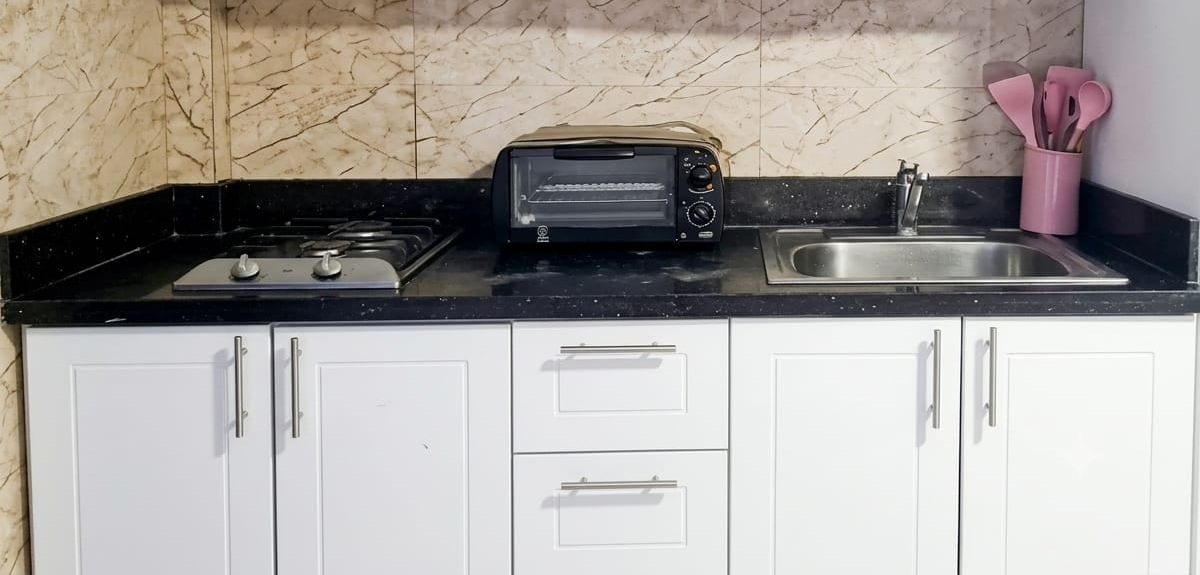Een keuken met een zwart aanrecht, witte kastjes, een toasteroven en een spoelbak.