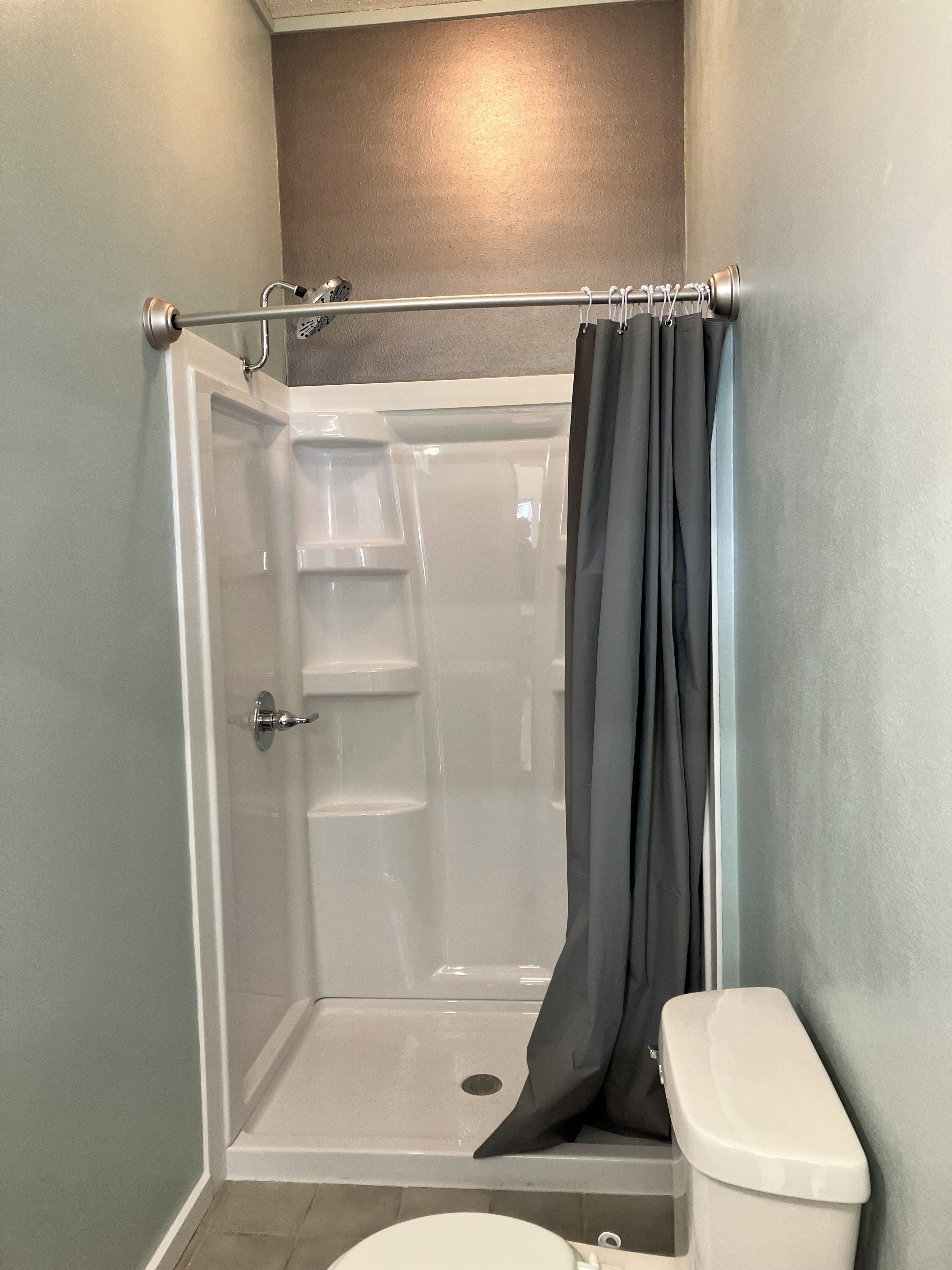 Une cabine de douche avec une porte en verre, un rideau de douche et des toilettes.