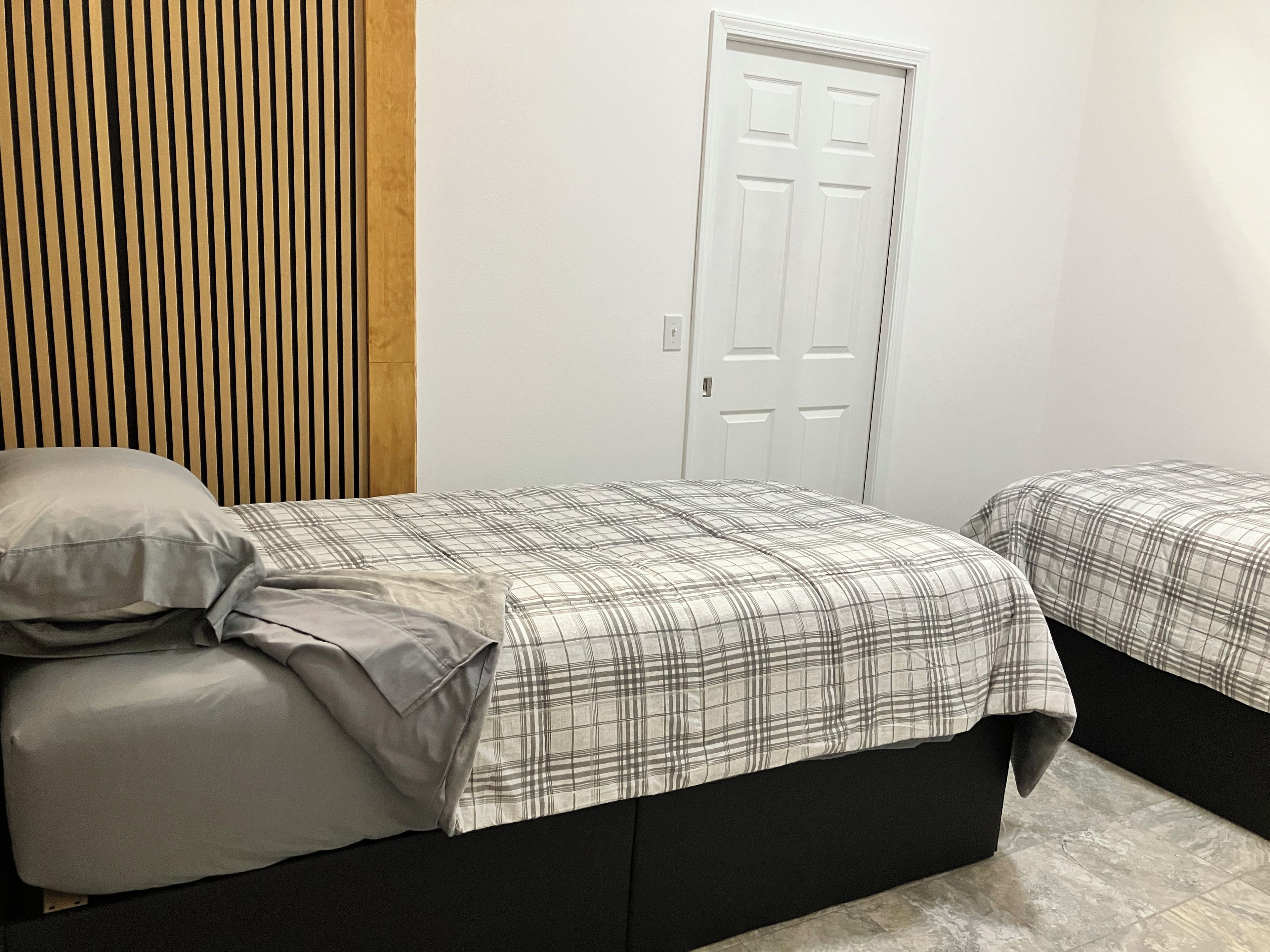 A bedroom with two beds, a wooden headboard, a white door, and a tiled floor.