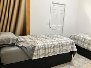 A bedroom with two beds, a wooden headboard, a white door, and a tiled floor.