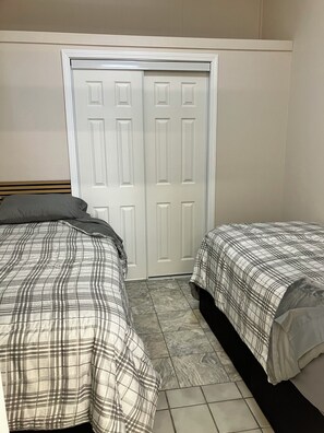 A bedroom with two beds, a wardrobe, and a tiled floor.