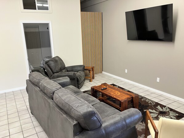 A living room with a grey sectional sofa, a wooden coffee table, and a flat-screen TV mounted on the wall.