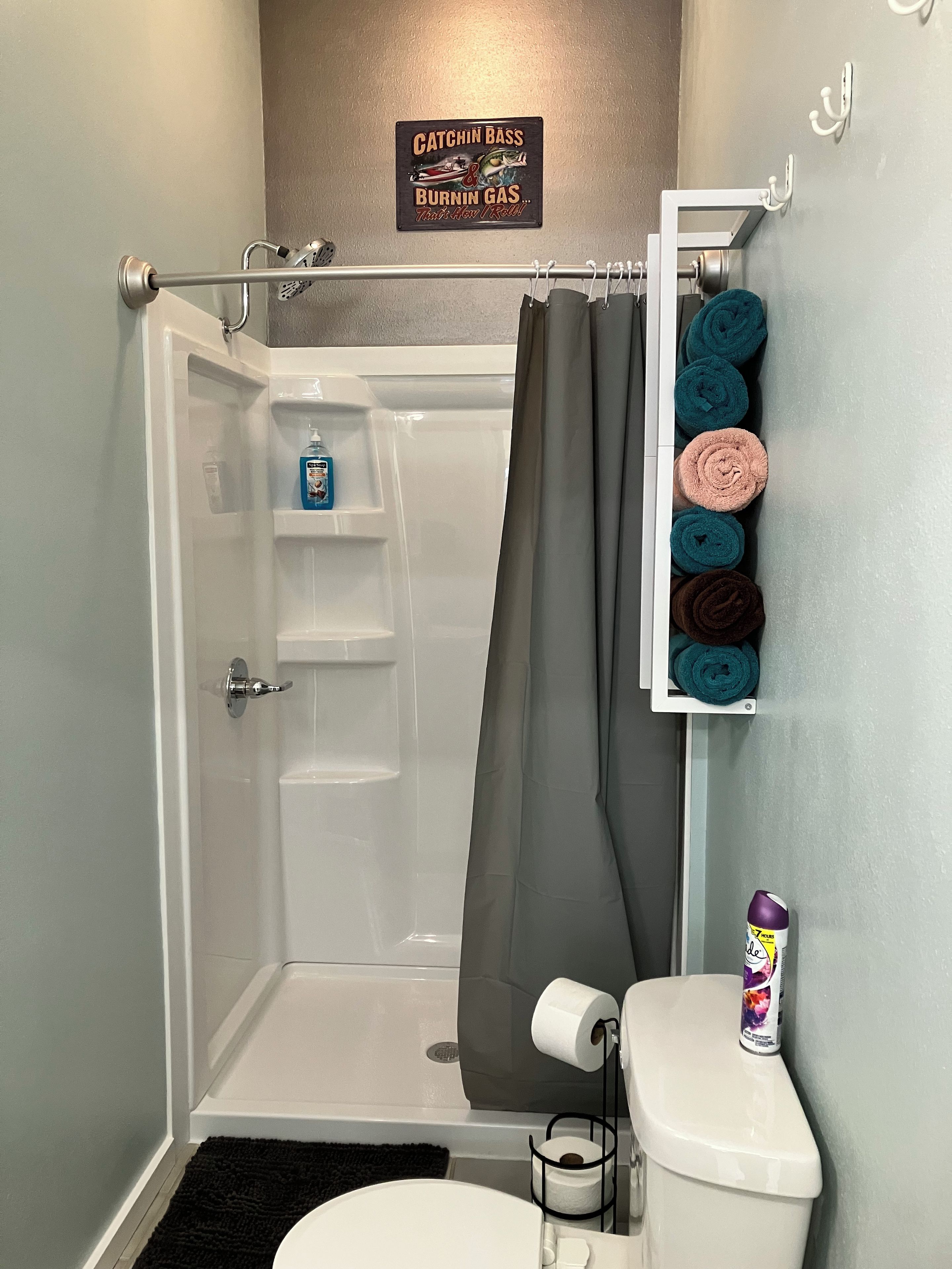 A bathroom with a shower, toilet, and a towel rack with towels.