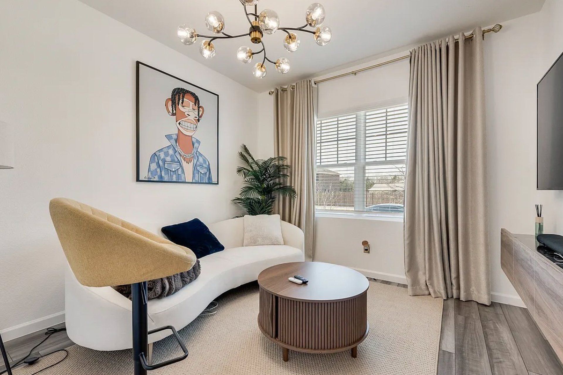 A modern living room with a white sofa, a round coffee table, a painting on the wall, and a large window with curtains.