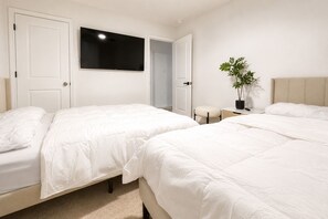 Une chambre avec deux lits, une télévision, une plante en pot et un petit tabouret.