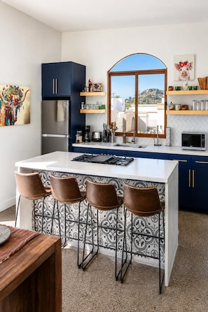 A modern kitchen with a central island, bar stools, and a view through a large window. - Private+Home+Oceanviews+Pool+Jacuzzi Getaway Near Valle de Guadalupe (Ensenada)