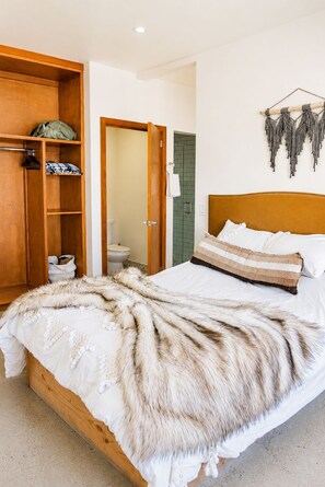 Ein Schlafzimmer mit einem hölzernen Bett, einem Fellüberwurf, einem Kleiderschrank und einer Wanddekoration aus Makramee.