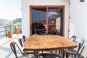 Ein Essbereich mit einem großen Holztisch und Stühlen, eine Schiebetür zu einem Balkon mit Blick auf eine Stadtlandschaft.