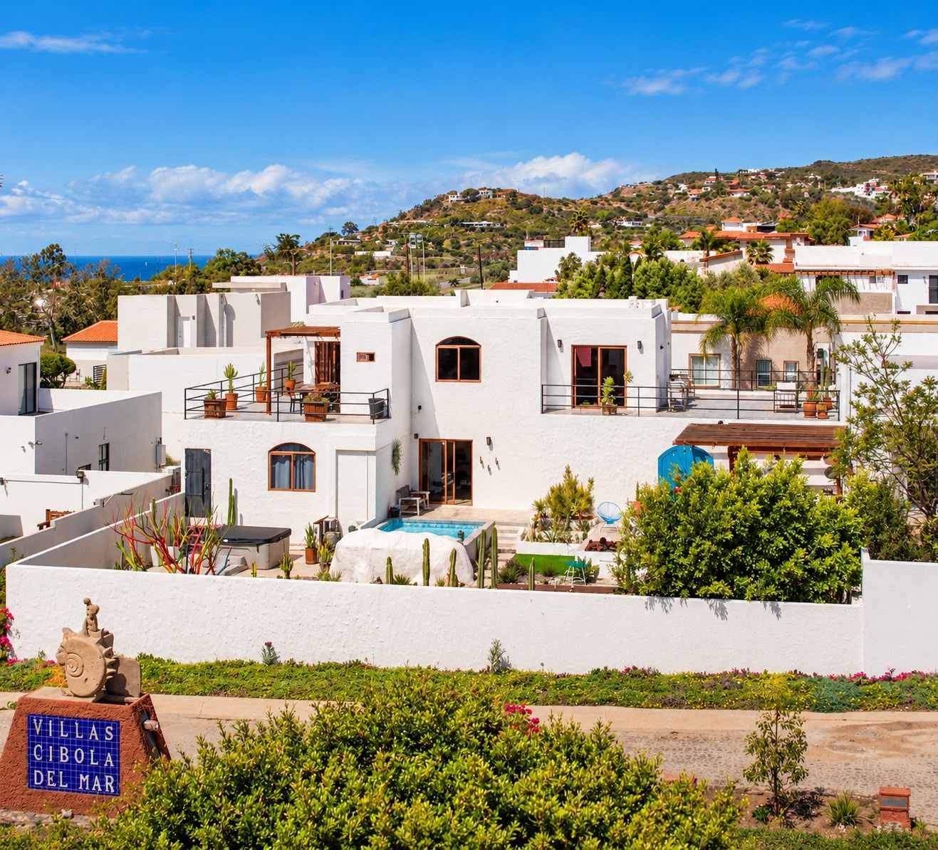 A coastal residential area with white buildings, a swimming pool, and a sign reading 'VILLAS CIBOLA DEL MAR'.