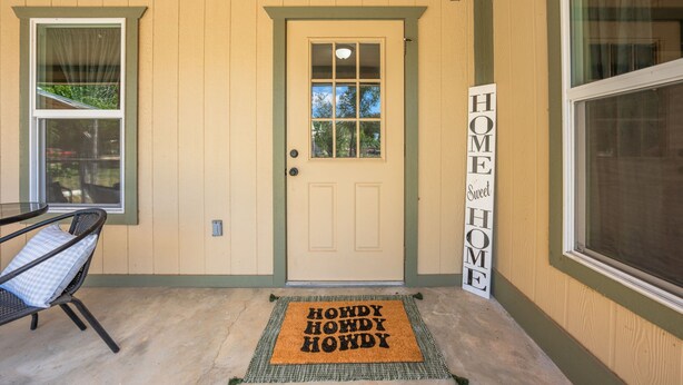 Eine Haustür mit einem 'HOME Sweet HOME'-Schild, einer Fußmatte und einem Stuhl davor.