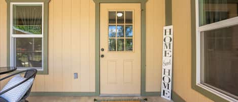 A front door with a 'HOME Sweet HOME' sign, a doormat, and a chair outside.