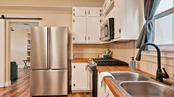 A modern kitchen with stainless steel appliances, wooden flooring, and white cabinetry.