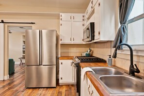 A modern kitchen with stainless steel appliances, wooden flooring, and white cabinetry.