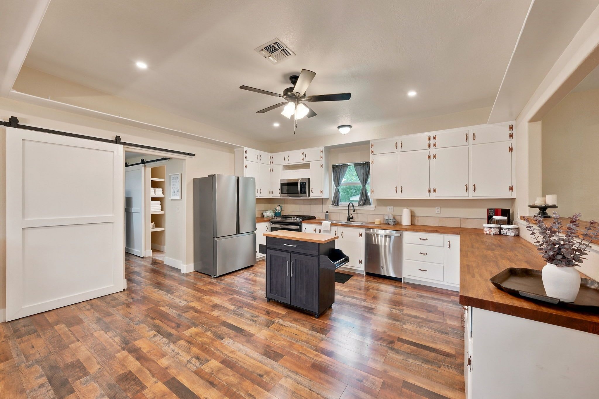 A modern kitchen with wooden flooring, white cabinets, a stainless steel refrigerator, a microwave, and a dishwasher.
