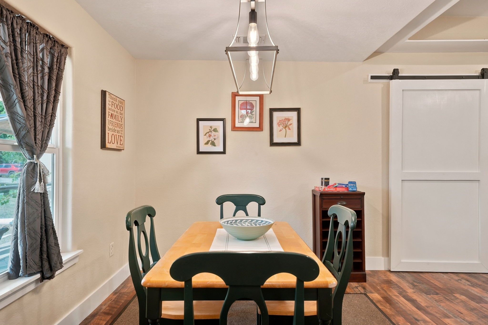 A dining room with a wooden table, green chairs, a bowl, framed artwork, and a sliding door.