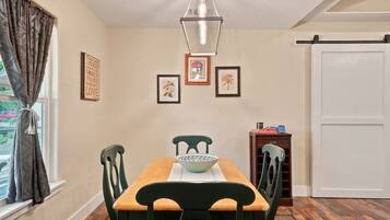 A dining room with a wooden table, green chairs, a bowl, framed artwork, and a sliding door.