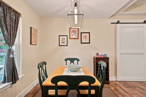 Comedor con mesa de madera, sillas verdes, un tazón, obras de arte enmarcadas y un puertas correderas.