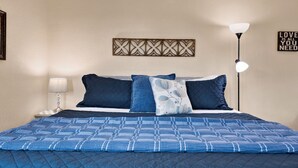 Ein ordentlich bezogenes Bett mit einer blauen Steudecke, einem dekorativen Wandpaneel, einem an der Wand befestigten Schild und einer Nachttischlampe.
