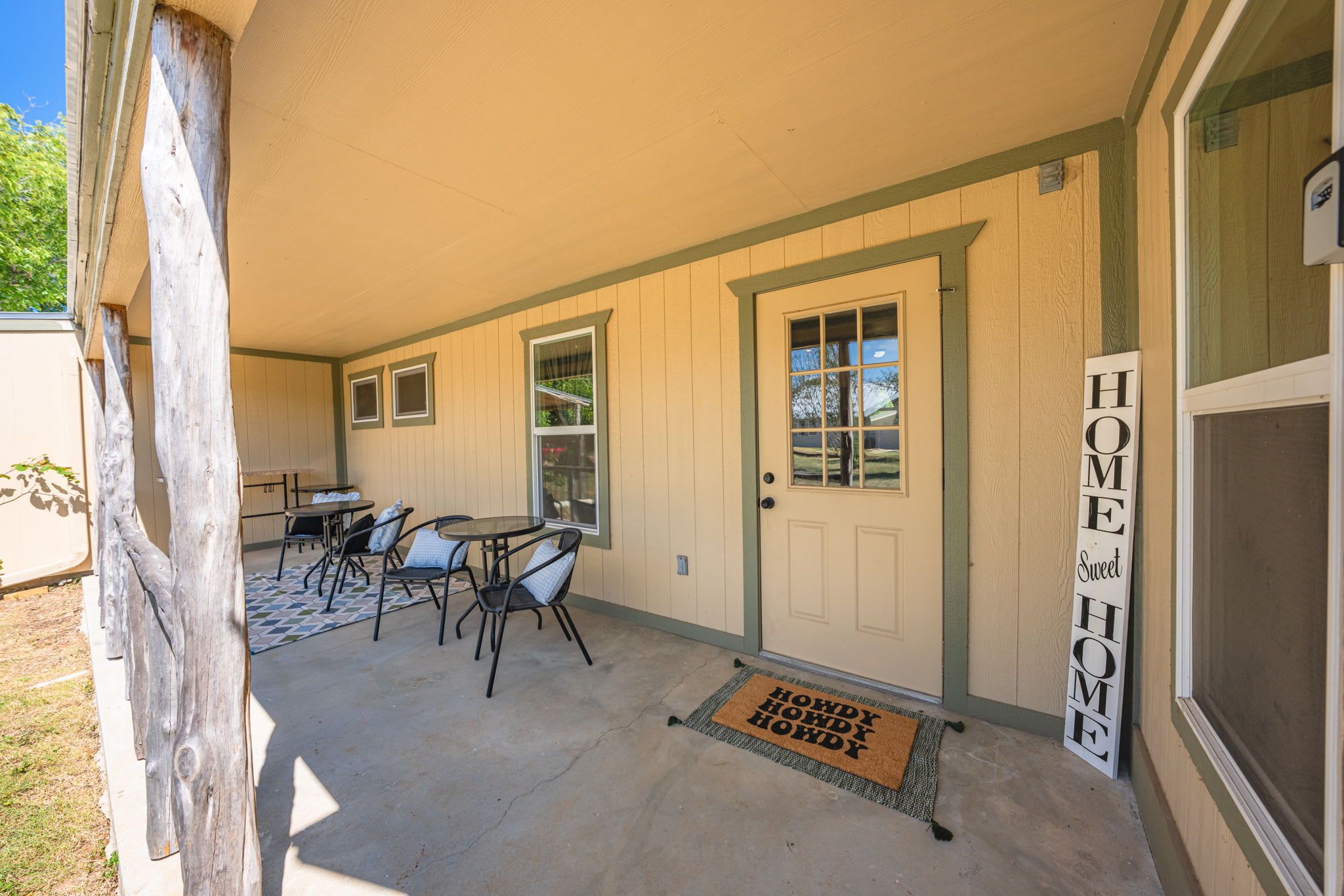 A covered patio area with a table and chairs, a door with a window, and a welcome mat.