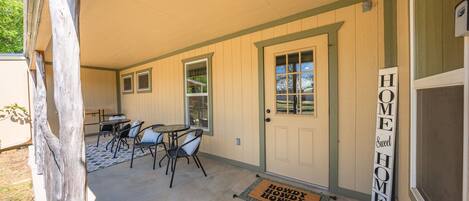 A covered patio area with a table and chairs, a door with a window, and a welcome mat.