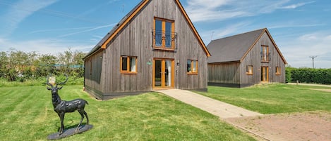 A wooden house with a balcony, a driveway, and a deer statue.