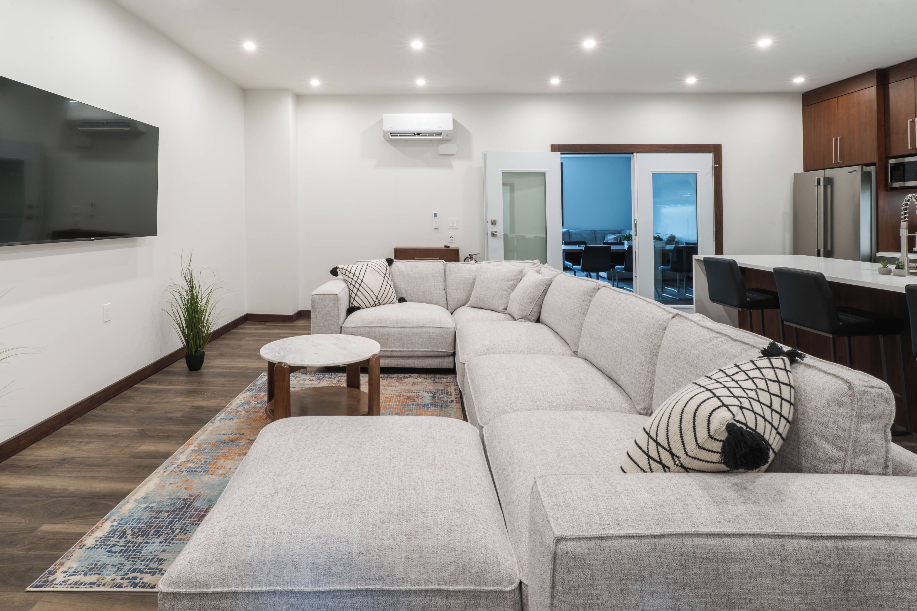 A modern living room with a sectional sofa, a small round table, and a large window overlooking a cityscape.