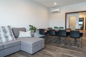 Ein modernes Wohnzimmer mit einem grauen Ecksofa, einem Esstisch mit Stühlen und einem großen Spiegel.