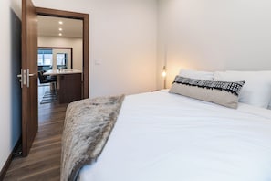 A hotel room with a bed, a wooden door, a bathroom, and a view of the outside. - The Timber Den (Revelstoke)