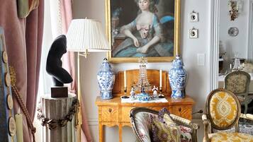 A room with a vintage aesthetic, featuring a classic armchair, a wooden side table with decorative items, and a framed portrait on the wall.