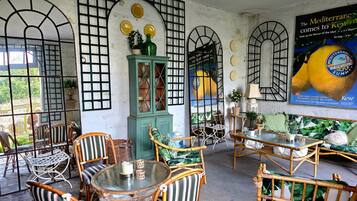 A room with wicker furniture, a glass table, and a poster advertising a Mediterranean summer event.
