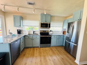 A modern kitchen with light blue cabinets, stainless steel appliances, and a wooden floor. - 3 Bedroom/Sleeps 7/Sea Isle/pool access (Galveston)