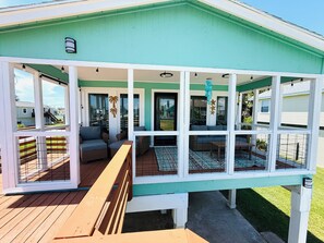 A covered outdoor seating area with multiple chairs and tables, a wooden deck, and a view of the surrounding neighborhood. - 3 Bedroom/Sleeps 7/Sea Isle/pool access (Galveston)
