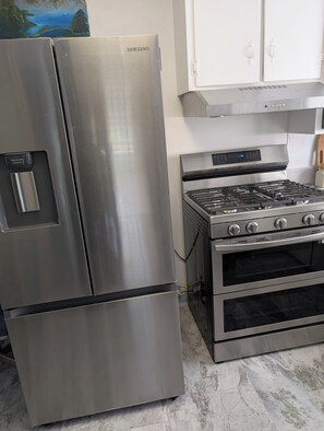 A stainless steel Samsung refrigerator and a built-in gas range with oven, in a kitchen with white cabinets and marble flooring.