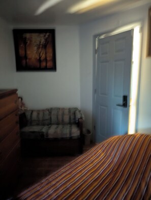 A bedroom with a bed, a dresser, a couch, and a door.