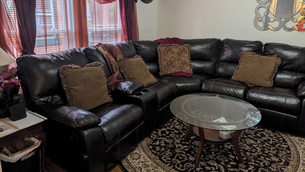 A living room with a black leather sofa, a glass coffee table, a patterned rug, and a wall clock. - 144H A Purple Portal Spacious 5-bedroom apartment (New London)