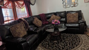 A living room with a black leather sofa, patterned throw pillows, a glass coffee table, and a decorative mirror on the wall. - 144H A Purple Portal Spacious 5-bedroom apartment (New London)