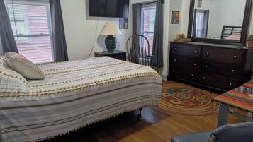 A bedroom with a bed, a dresser, a chair, a lamp, and a TV.