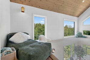 Ein modernes Schlafzimmer mit Bett, großen Fenstern und Blick auf Grün.