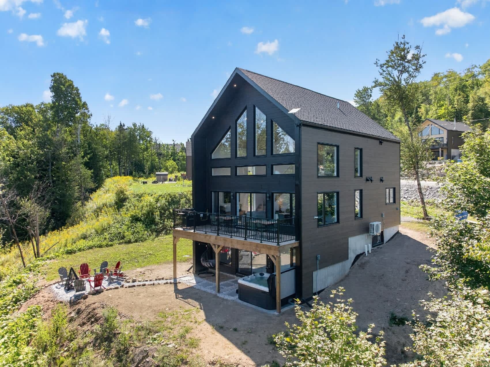 A modern two-story house with a large balcony, surrounded by a garden and trees.