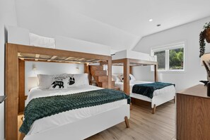 Ein Schlafzimmer mit zwei Etagenbetten, einem Schreibtisch und einem Fenster mit Blick auf Grünflächen.