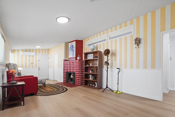 Ein Wohnzimmer mit Kamin aus roten Ziegeln, Streifenmuster-Tapete und einem roten Sofa.
