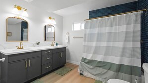 Een moderne badkamer met een witte wastafel, donkere kastjes, gouden details en een gestreept douchegordijn.