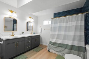 Ein modernes Badezimmer mit einem weißen Waschtisch, dunklen Schränken, goldenen Armaturen und einem gestreiften Duschvorhang.