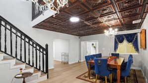 Een ruime eethoek met een houten tafel en blauwe fauteuils, een kroonluchter en een houten trap met zwarte spijlen.
