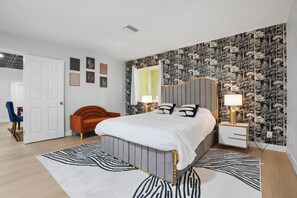 Ein Schlafzimmer mit Bett, Nachttischen, einem Sessel und einer Tür.